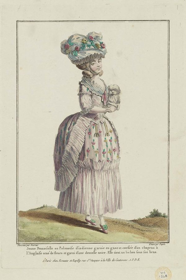 French : Jeune Demoiselle en Polonoise d’indienne garnie en gaze et coeffée d’un chapeau à l’Angaise orné de fleurs et garni d’une dentelle noire. Elle tient un bichon sous son bras.